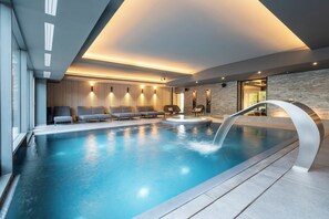 Una piscina interior moderna con una cascada, zona de estar con tumbonas y una pared de piedra.