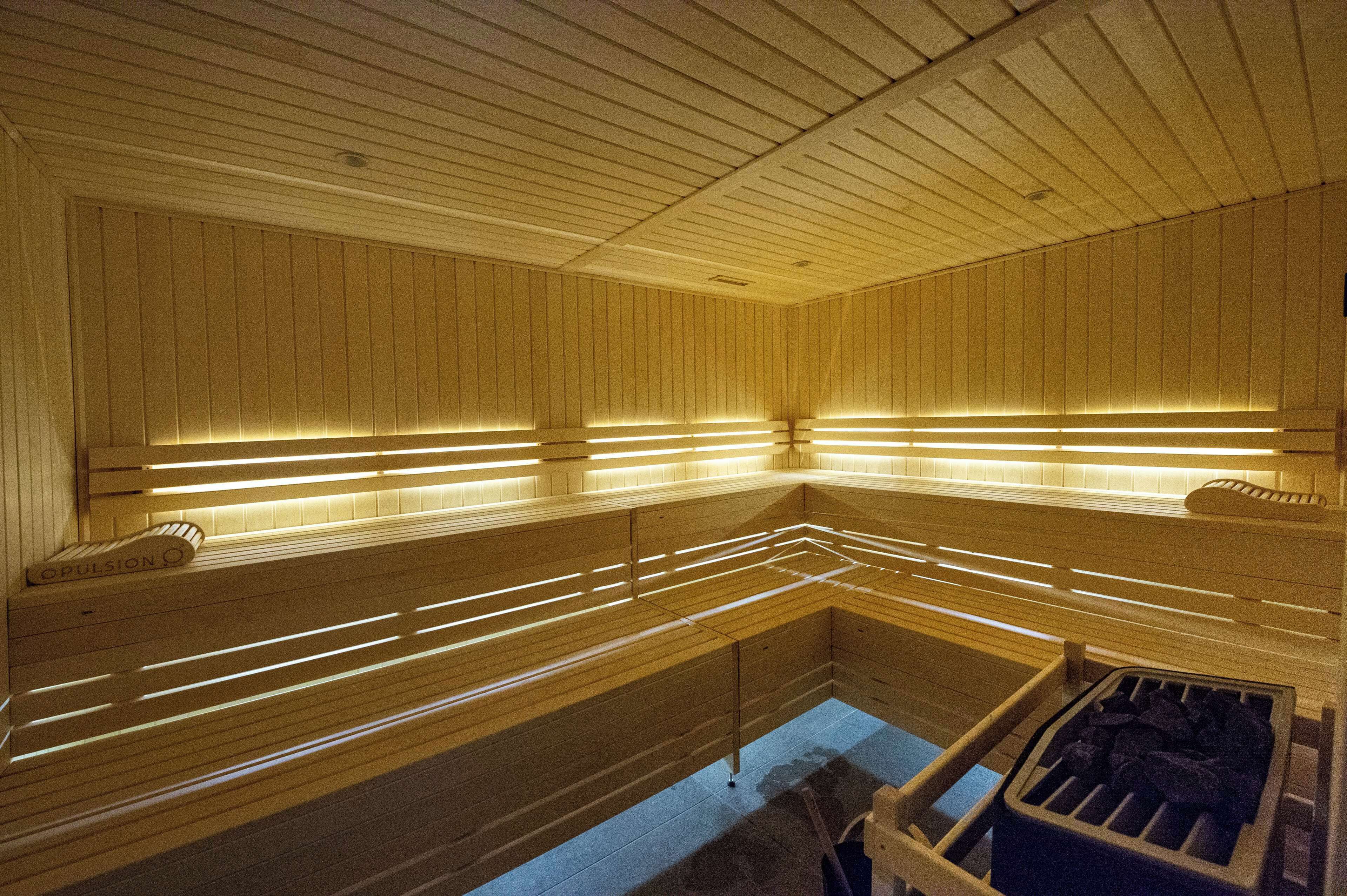 Un sauna avec des bancs en bois et des parois à lattes, éclairé par des luminaires linéaires.