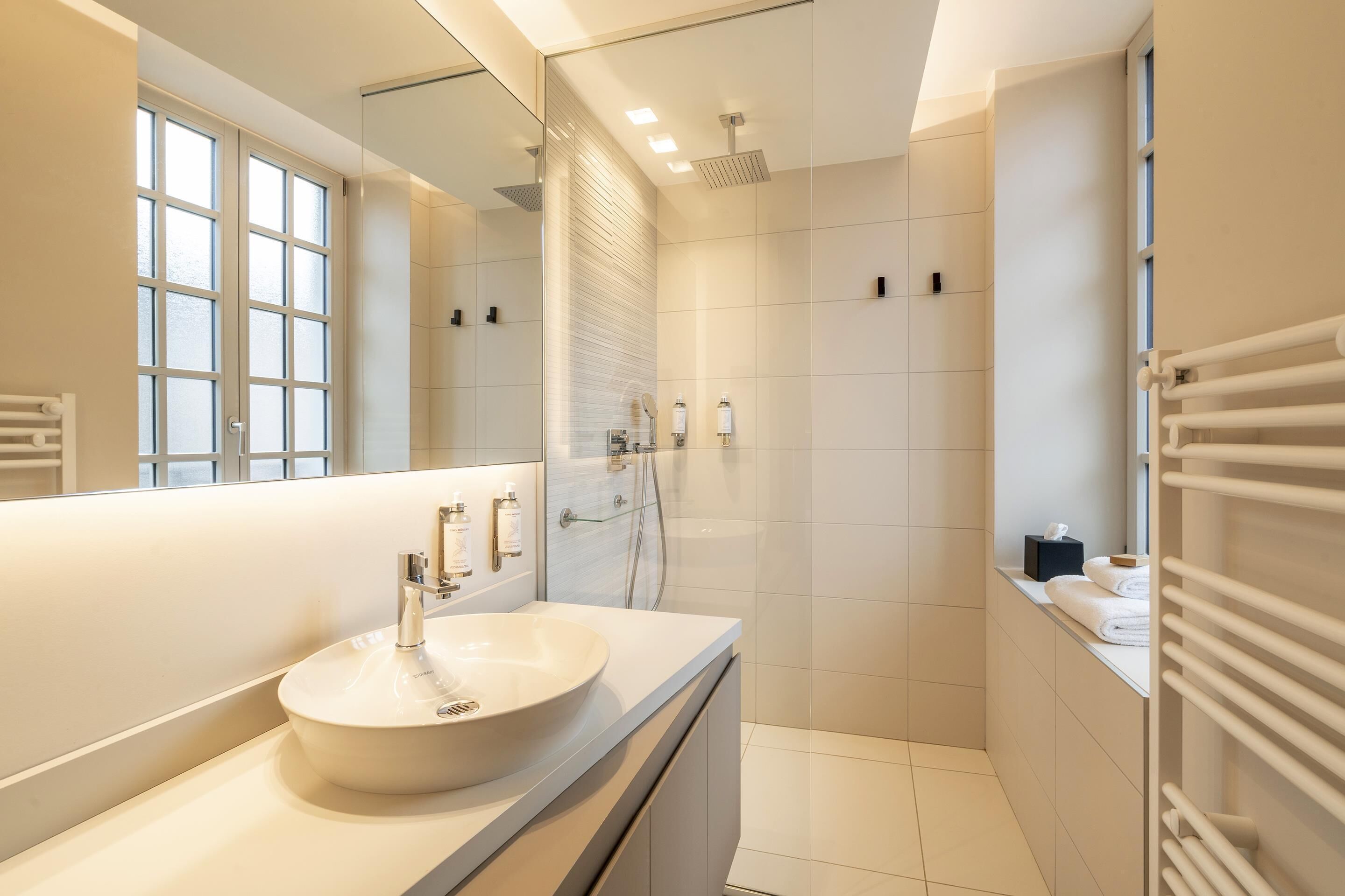 Un baño moderno con un espejo grande, un lavabo blanco, ducha y toallero.