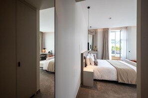 Una habitación de hotel moderna con una cama grande, una mesita de noche, un espejo y una ventana con cortinas.