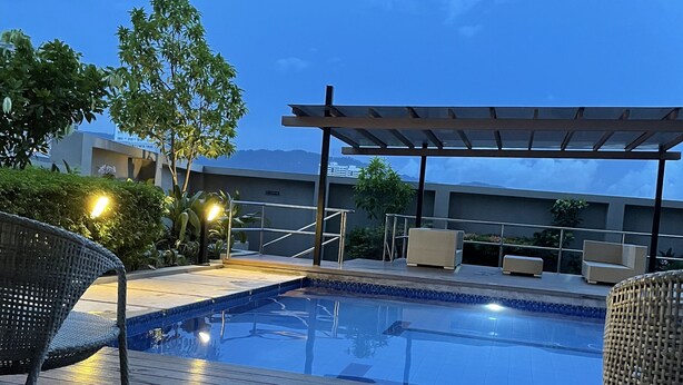 An outdoor swimming pool with wooden decking, surrounded by wicker chairs and a pergola.
