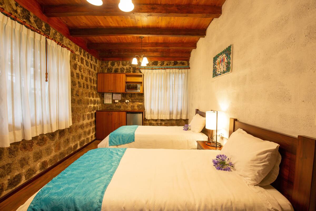 Quarto com duas camas, uma kitchenette e uma parede de pedra.