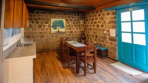 A rustic dining area with a wooden table and chairs, a stone wall, and a blue door. - Niebli Historical Farm and Lodge at Pululahua Volcano (Calacali)