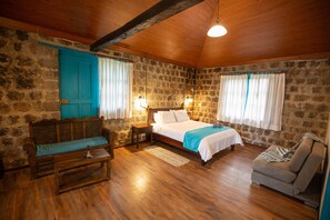 Una habitación acogedora con techo de madera, paredes de piedra, una cama con ropa de cama blanca, un sofá azul y un sillón gris.