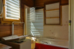 Une salle de bain avec une baignoire, une fenêtre avec des stores et un porte-serviettes.