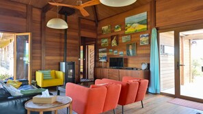 A wooden cabin interior with a sofa, chairs, a TV, and artwork on the walls.