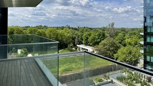 Un bâtiment moderne doté d’un balcon en verre qui offre une vue imprenable sur un paysage verdoyant et un ciel dégagé.