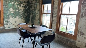 A room with a wooden table and four chairs, large windows with blinds, and a brick wall with peeling paint. - Downtown Luxury Condo for 2! (San Antonio)