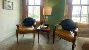 A room with two leather chairs, a small table with a lamp, and a view of the city through large windows. - Downtown Luxury Condo for 2! (San Antonio)