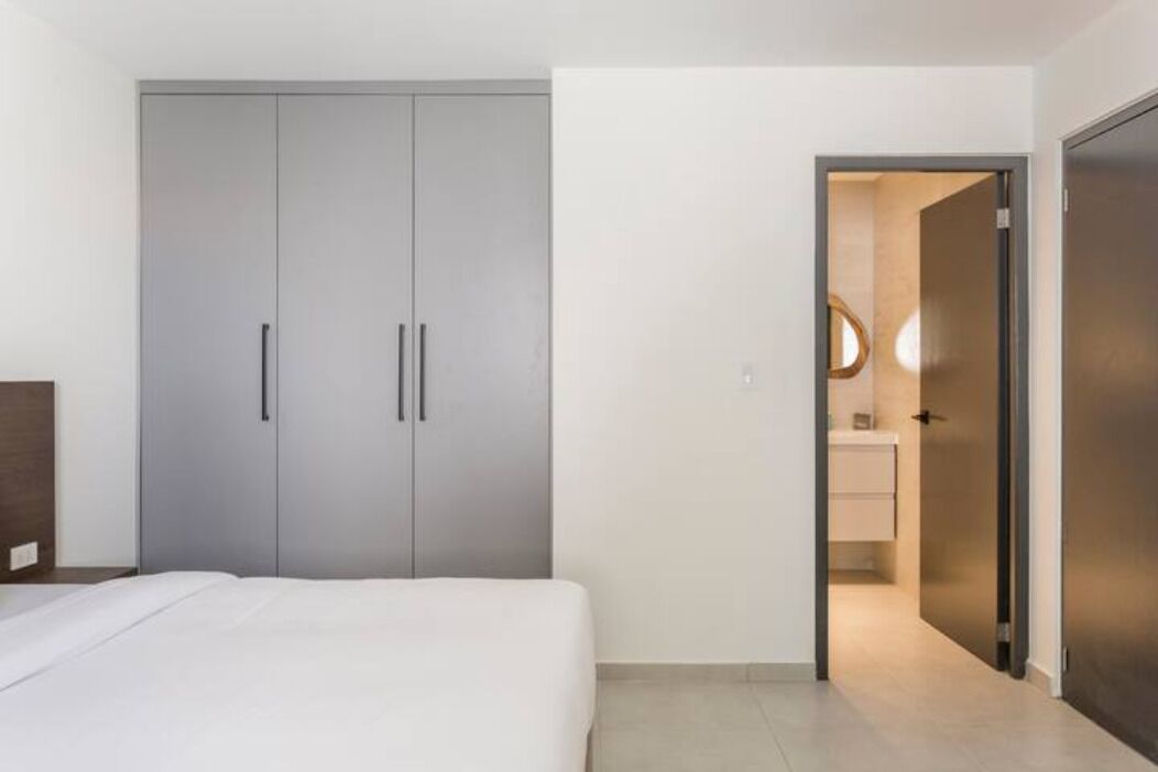 Een slaapkamer met een bed, een grijze garderobe en een badkamer die door een geopende deur zichtbaar is.