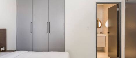 Een slaapkamer met een bed, een grijze garderobe en een badkamer die door een geopende deur zichtbaar is.