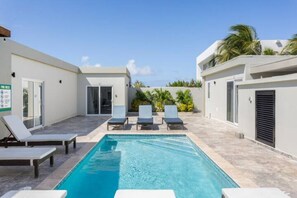 A swimming pool with lounge chairs, a clear sky, and a building with a door and windows. - Emerald 1BR APT -#E1 in Noord-Sleeps 2 (Noord)