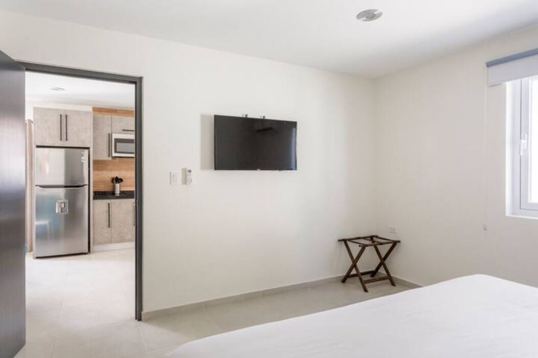 A modern, minimalistic bedroom with a bed, a small wooden table, and a TV mounted on the wall.