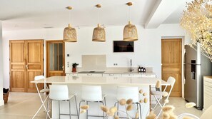 Una cucina moderna con isola centrale, sedie bianche e lampade a sospensione in vimini.