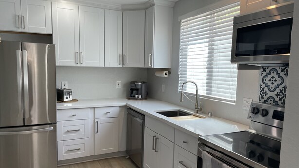 Een moderne keuken met roestvrijstalen apparatuur, witte kasten, een inbouwoven en een raam met jaloezieën.