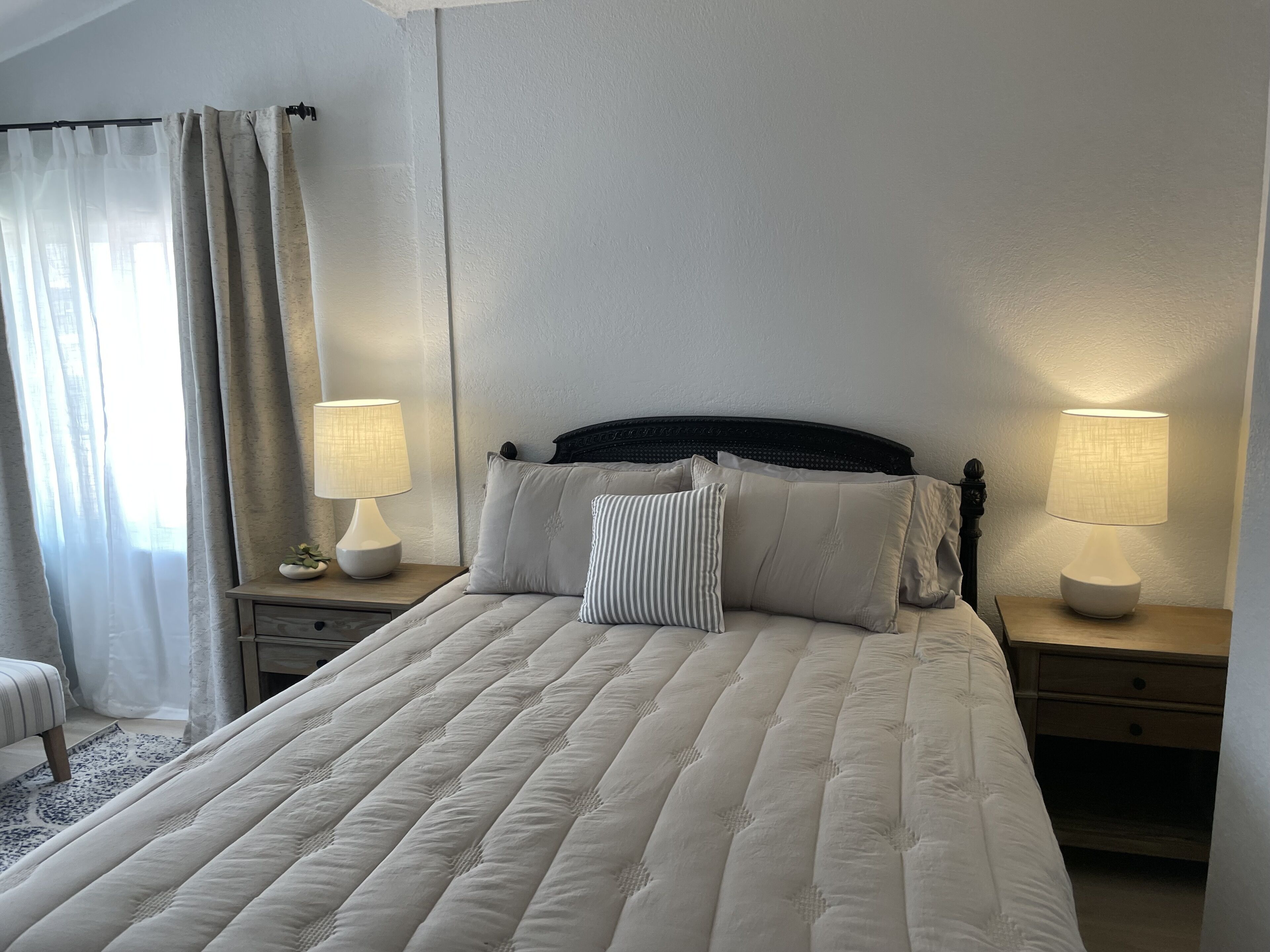 Ein ordentlich bezogenes Bett mit einer gesteppten Decke, zwei Nachttischlampen und einem Nachttisch mit Lampe.