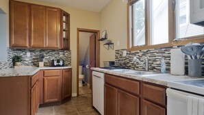 A kitchen with wooden cabinets, a tiled backsplash, and a window above the sink. - Nauvoo Family Home 15 Minutes From Temple (Hamilton)