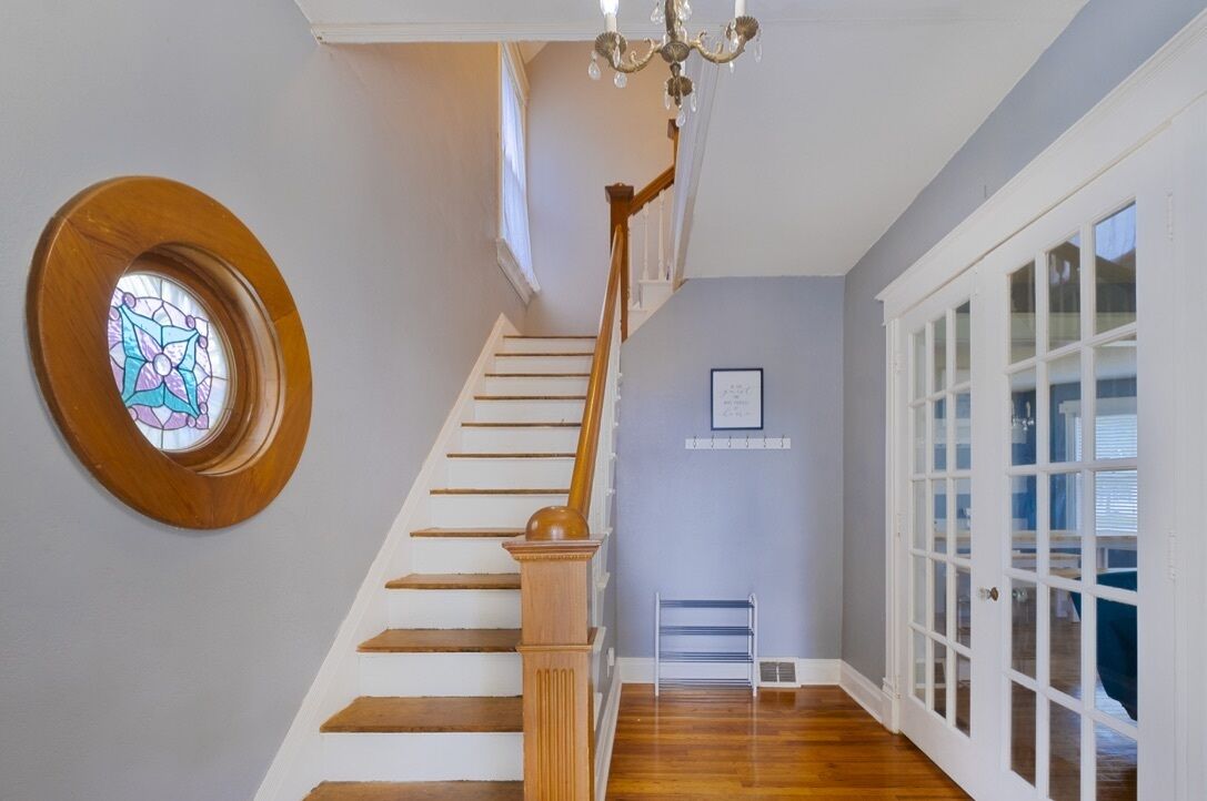 Un escalier avec des marches en bois et une rampe en bois, menant à une pièce dotée d’une grande fenêtre et d’une porte à panneaux de verre.