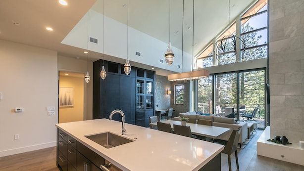 Une cuisine moderne dotée d’un îlot central, de luminaires suspendus et d’un coin repas offrant une vue sur l’extérieur.