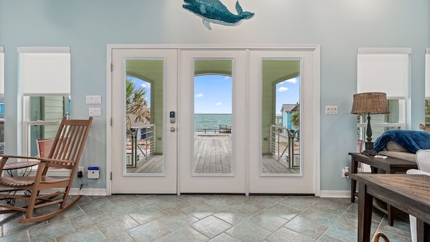 A room with a wooden rocking chair, a table, and a view of the ocean through a glass door.