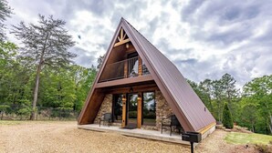 Una cabaña moderna tipo A con base de piedra, grandes puertas de vidrio y un balcón.