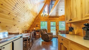 Un acogedor interior de cabaña con comedor, sofá y cocina con armarios de madera y estufa.
