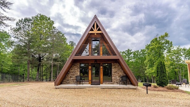 Un edificio moderno de forma triangular con fachada de piedra, un balcón y una pequeña zona de estar al aire libre.