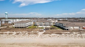 Un complexe hôtelier situé sur la côte, composé de plusieurs bâtiments, d’un château d’eau et entouré d’un terrain sablonneux.