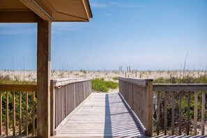 Een houten looppad dat naar een strand met duinen en schaarse begroeiing leidt.