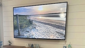 Un téléviseur à écran plat fixé au-dessus d’une étagère en bois, sur laquelle on peut lire le mot « PLAGE », et une cheminée avec un feu illuminé de bleu en dessous.