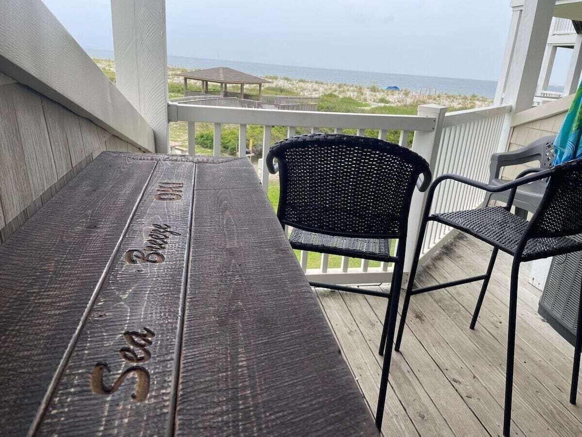 Um deck de madeira com uma mesa e duas cadeiras, com vista para uma praia e oceano.