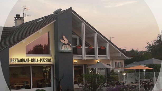 En restaurang med en skylt som visar en grill och en pizzeria, uteservering och en hjortstaty.