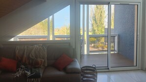 Ett rum med ett sluttande tak, en soffa med kuddar, en korg och en skjutdörr i glas som leder ut till ett utomhusområde.