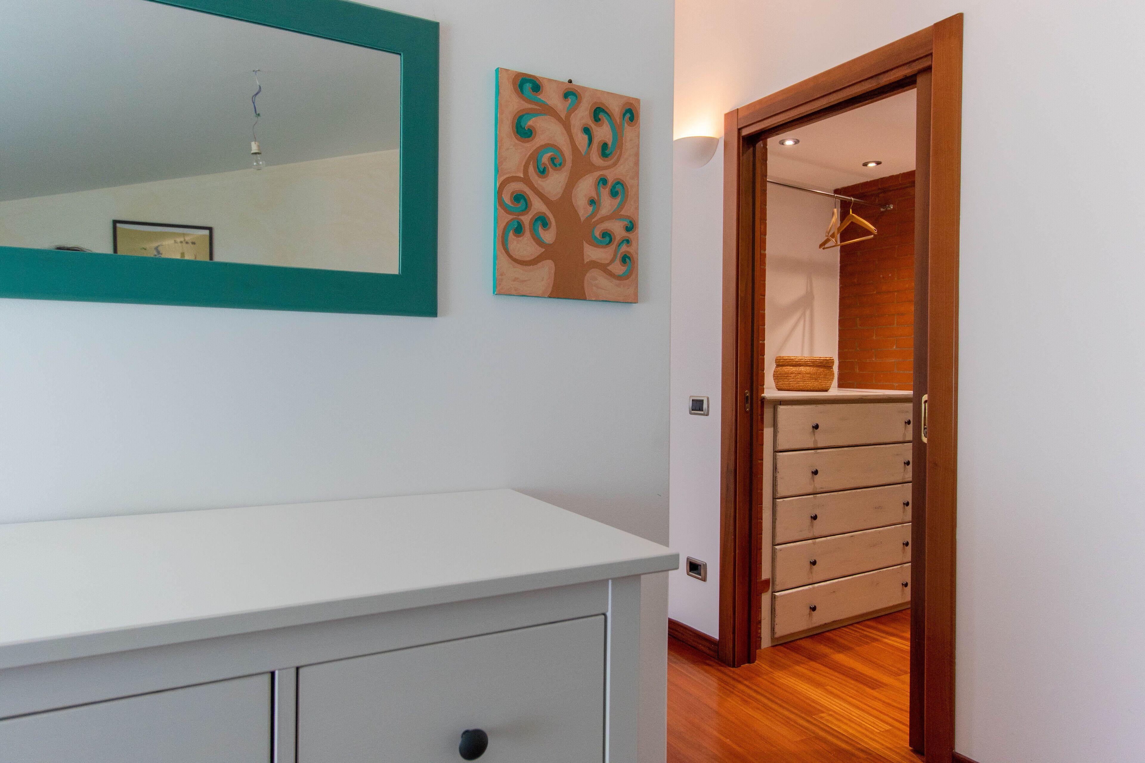 Una habitación con un aparador blanco, un espejo y una puerta de madera que da a un armario con una percha y cestas.