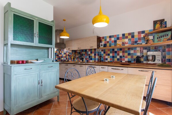 Una cocina con una mesa de madera, sillas azules, un armario verde y un salpicadero de azulejos coloridos.