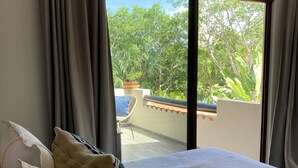 Un dormitorio con una cama grande, cortinas grises y vistas a un balcón con plantas y árboles.