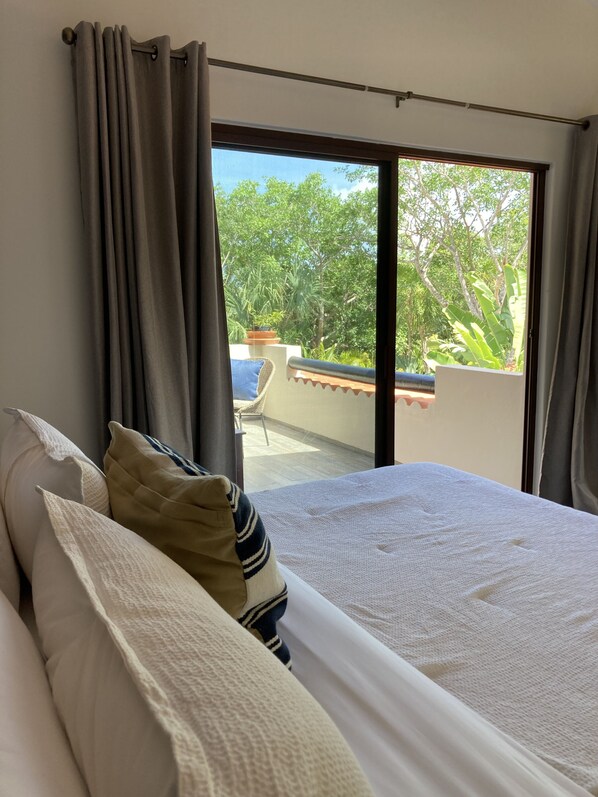 A bedroom with a large bed, grey curtains, and a view of a balcony with plants and trees. - Spacious Private Villa with Pool Backing to Golf Course Beach Only Minutes Away (Puerto Aventuras)