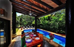 An outdoor dining area with a pool, surrounded by lush greenery.
