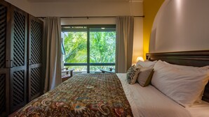 Habitación de hotel con una cama grande, vista a palmeras a través de una puerta corrediza y cabecero de madera.