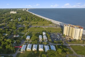 Vista aérea de una zona costera con playa, estacionamiento y un hotel con varios edificios.