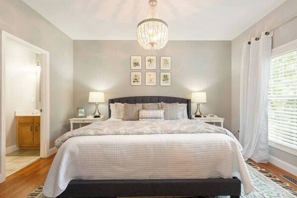 A bedroom with a large bed, two bedside tables, a chandelier, and framed botanical prints on the wall.