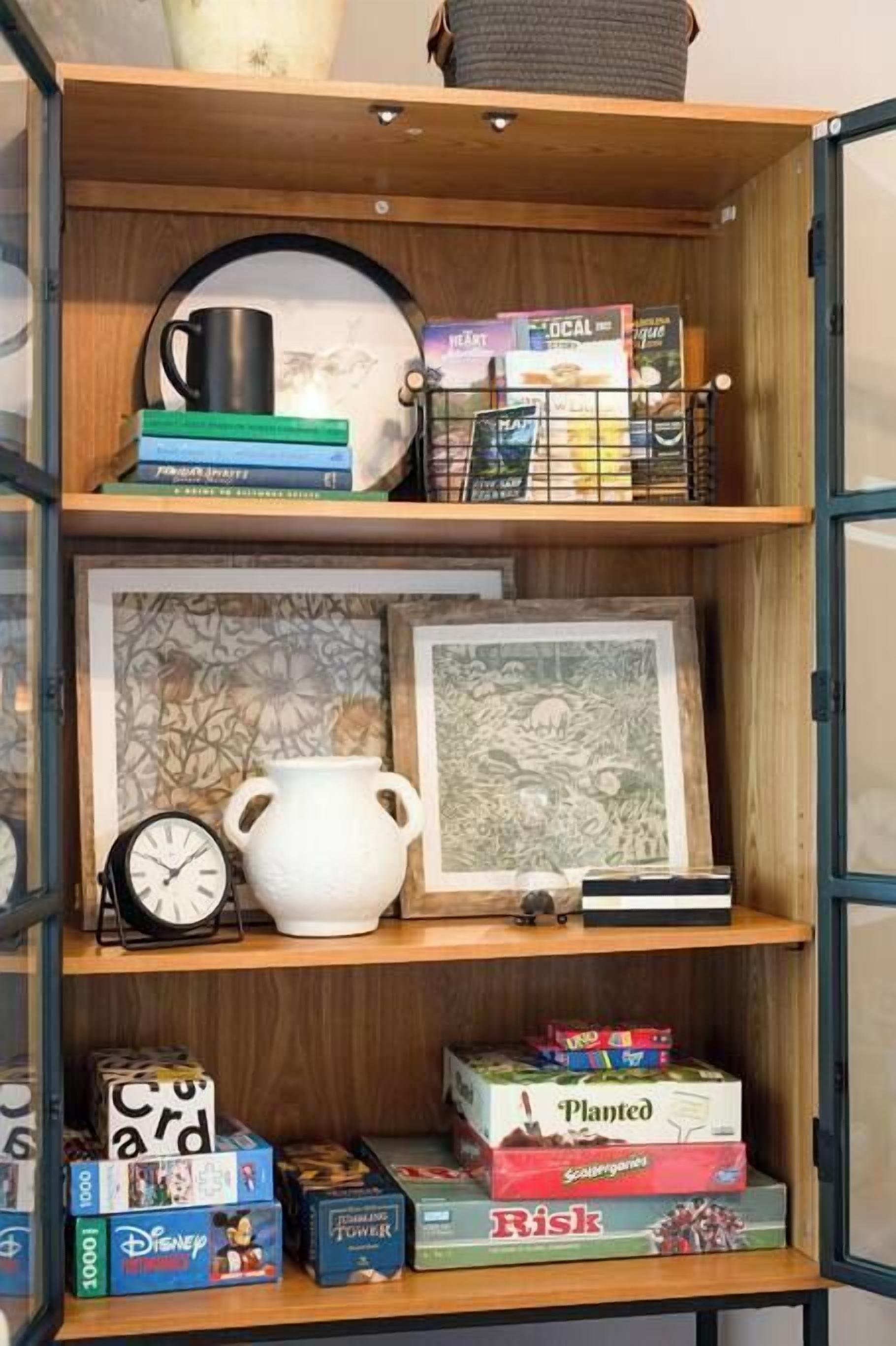 A wooden shelf with books, a mug, a clock, framed artwork, and board games.