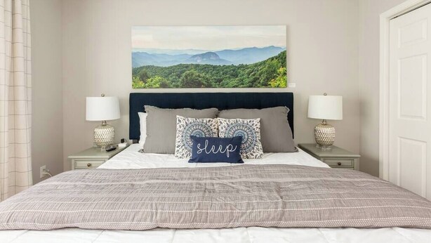 A bedroom with a large bed, two bedside tables with lamps, a headboard with a landscape painting, and a pillow with the word "sleep". - *10 Minutes to Downtown & Biltmore, Next to Parkway (Asheville)