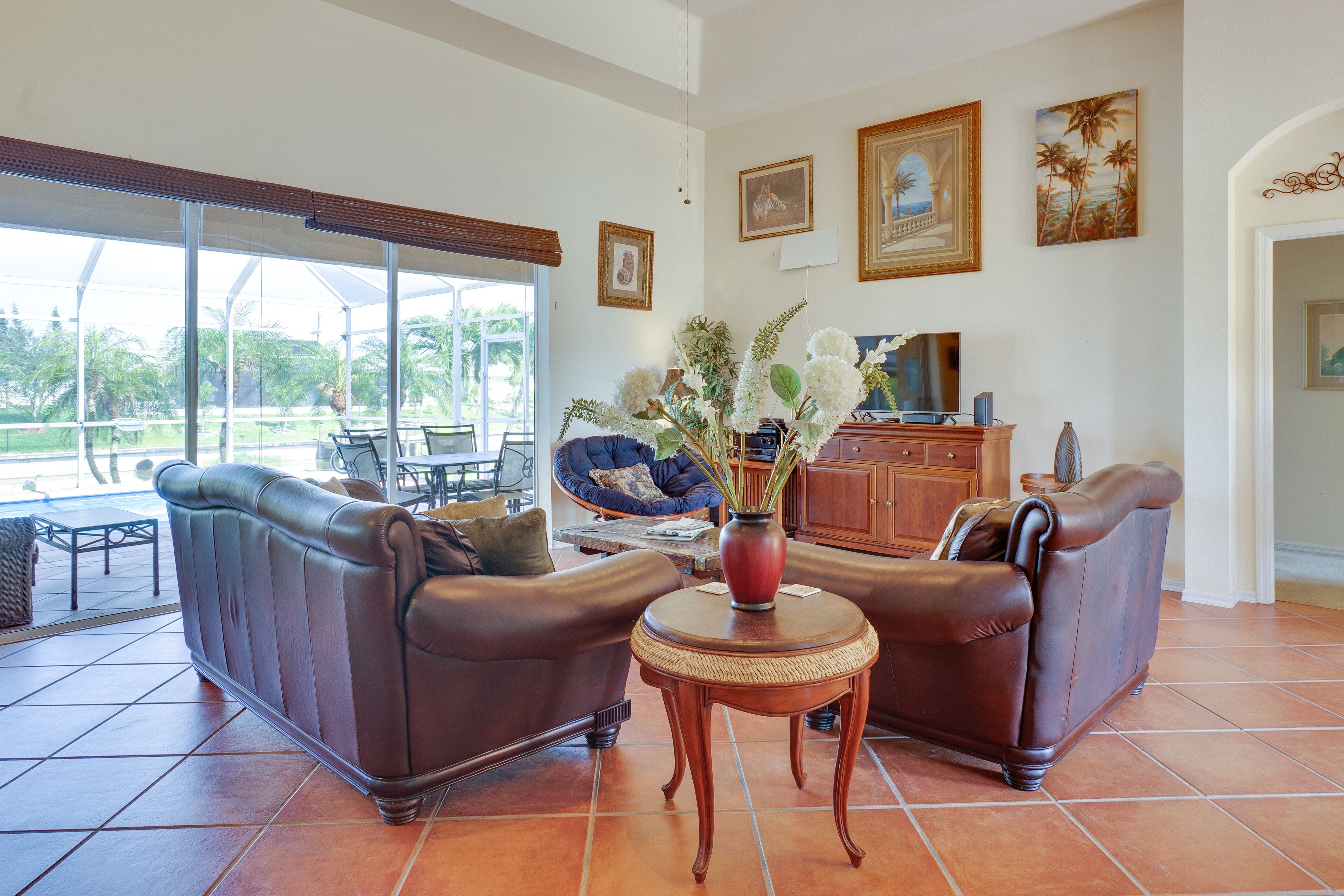 A spacious living area with a large window, a brown leather sofa, a small round wooden table, and a cabinet.