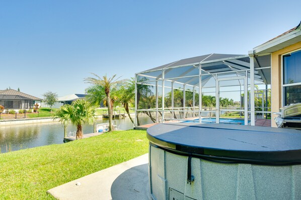 Área externa coberta com piscina, palmeiras e vista para a água.