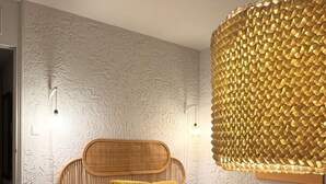 A bedroom with a textured wall, a wooden headboard, a bed with white bedding, and a unique textured light fixture.