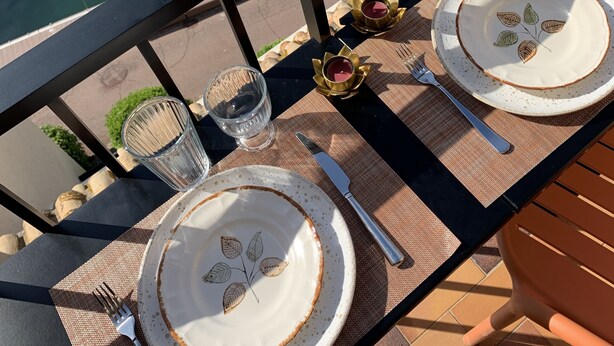A table set with plates, glasses, and cutlery on a terrace overlooking a body of water with a boat in the background.
