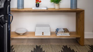 A hallway with a wooden console table, a mirror, two lamps, a vase with flowers, a book titled 'American', and a bowl. - Modern, Spacious Pool Home in Plano (Plano)