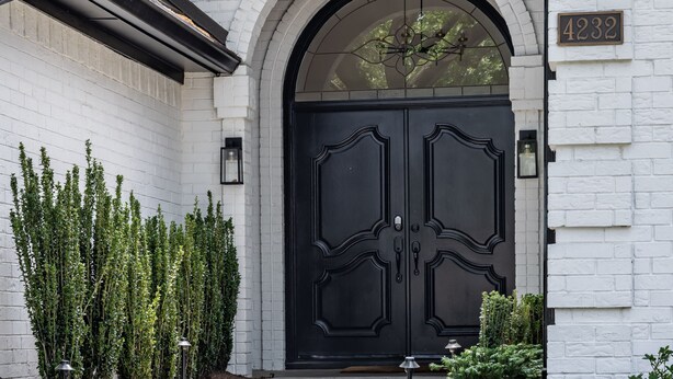 A white brick building with a black double door, a small garden with flowers, and a clear pathway leading to the entrance. - Modern, Spacious Pool Home in Plano (Plano)
