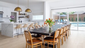 A modern kitchen with white cabinets, a marble island, and a dining area with a dark table and wicker chairs. - Modern, Spacious Pool Home in Plano (Plano)